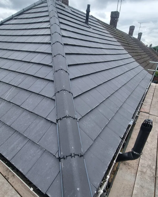 A line of clipped grey hip tiles running down the corner of a newly tiled roof to the gutter, with a brick chimney at the top
