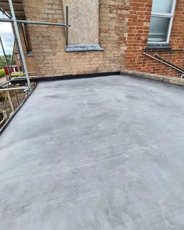 A smooth grey flat roof on a rear extension, finished with a black trim where it meets the brick walls, with scaffolding at one side