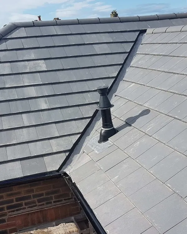 A newly tiled grey roof where two slopes meet in a lined valley, with a black vent pipe flashed into the tiles and capped ridges and hips