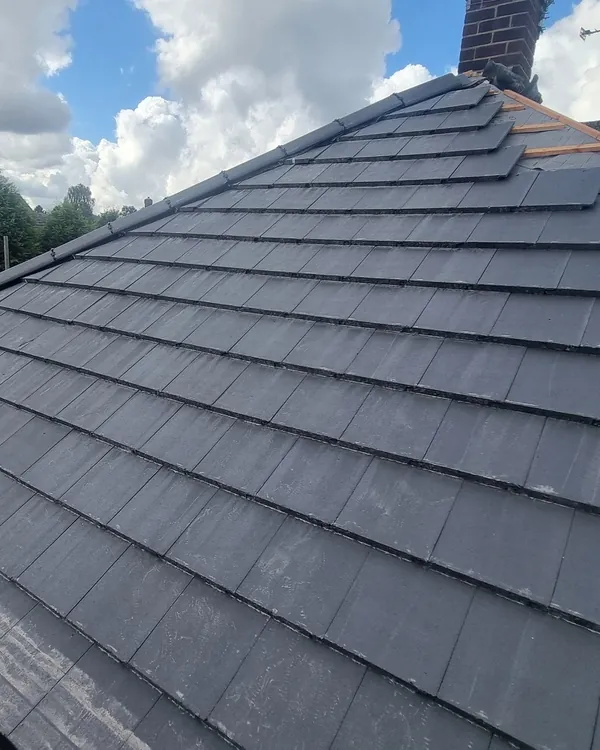 New grey interlocking tiles being laid on a hipped roof, with timber battens and membrane still showing near the ridge, seen from the scaffold