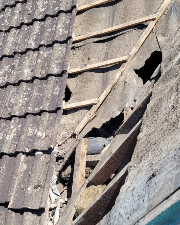 Old concrete tiles lifted to show torn, perished roofing felt with holes in it and broken timber battens underneath