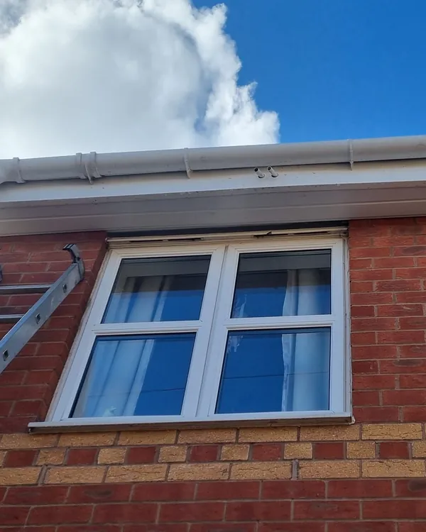 White uPVC fascia, soffit and guttering above the first-floor windows of a brick house, with a ladder to one side and blue sky